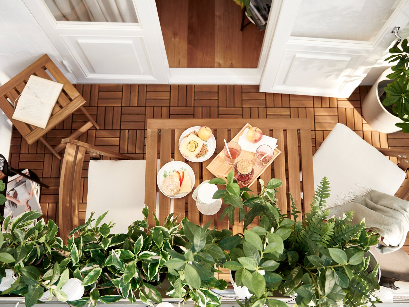 Un balcón decorado con láminas de acacia, presentes nos mobles NÄMMARÖ e o chan de exterior RUNNEN, e plantas artificiais FEJKA.