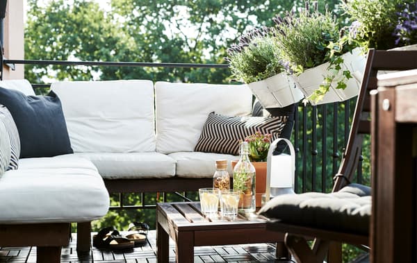 Un balcone con piante in vaso e mobili in legno scuro con cuscini bianchi - IKEA