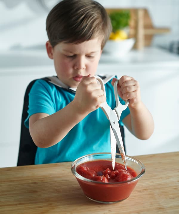 Un bambino che taglia dei pomodori pelati in una ciotola con le forbici.