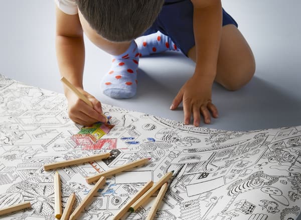 Un bambino colora dei disegni in bianco sul rotolo di carta LUSTIGT, usando le matite colorate MÅLA.