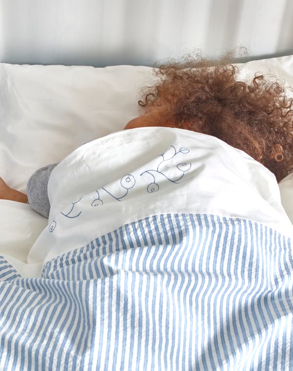 Un bambino dai capelli ricci dorme in un lettino con copripiumino e federa GULSPARV a righe bianche e blu - IKEA