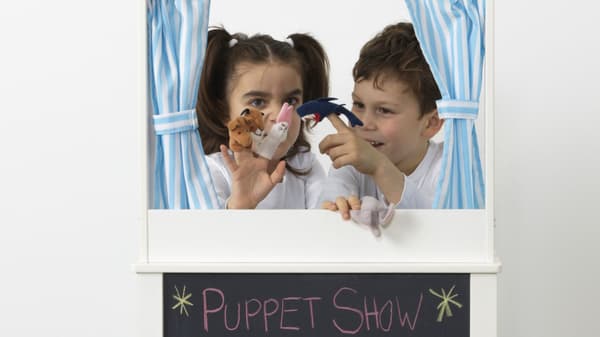 Un bambino e una bambina giocano con dei pupazzetti con sotto di loro una lavagna con scritto puppet show.