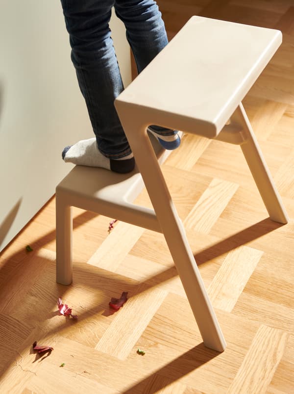 Un bambino in piedi sullo scalino più basso della scaletta/sgabello MÄSTERBY in una cucina. Sul pavimento, scarti di cipolla rossa - IKEA