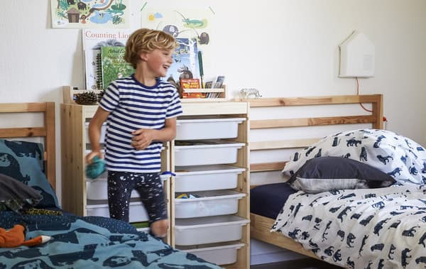 Un bambino in una cameretta con due letti affiancati, mobili in legno e tessili fantasia - IKEA