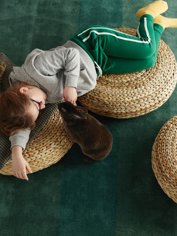 Un bambino sdraiato su pouf ALSEDA mentre dta accarezzando un coniglietto.