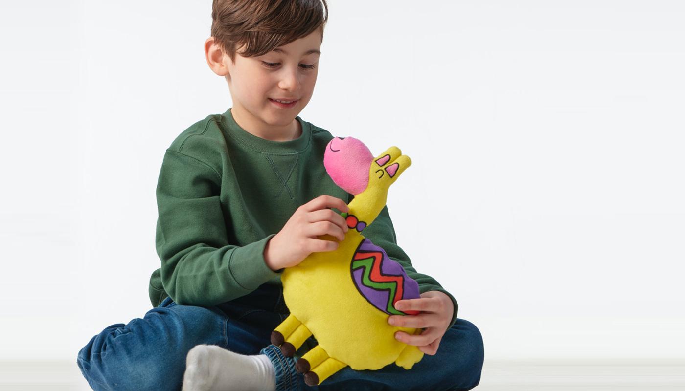 Un bambino seduto sul pavimento mentre tiene in mano un peluche SAGOSKATT.