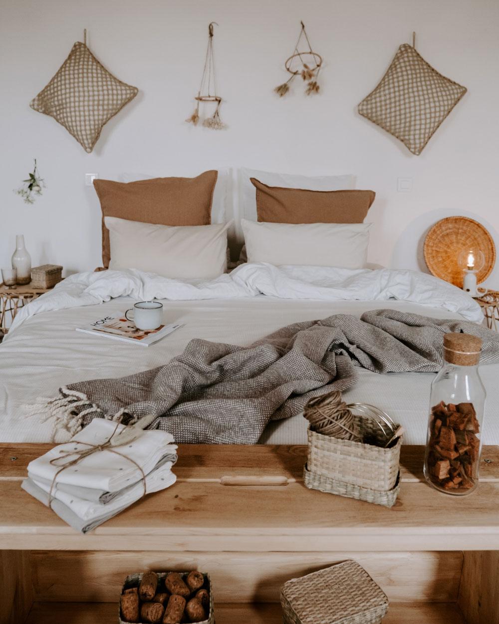 Un banc en bois disposé devant un lit deux places et quelques décoration suspendues au mur.