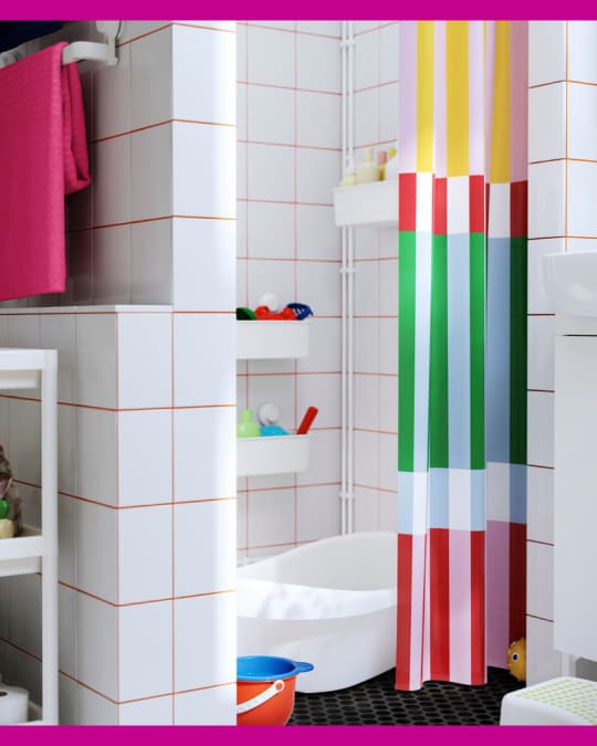 Un baño con baldozas blancas tiene una cortina de baño de colores verde, fucsia y amarillo.