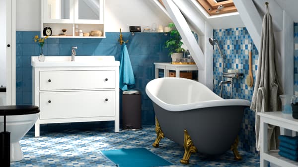 Un baño con suelo y azulejos azules, una bañera independiente y un lavabo blanco con armarios con espejos en la parte superior.