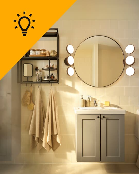 Un baño con un mueble parala lavamanos gris y sobre él un espejo redondo con luminarias KABOMBA.