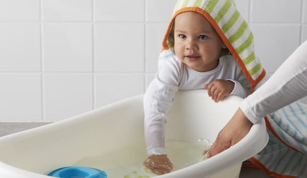 Un bebé con un arbornoz  mete las manos en una bañera de plástico blanco LÄTTSAM.