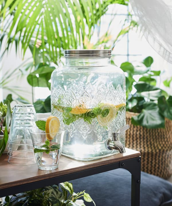 Un bicchiere riempito con della bevanda proveniente dal dispenser con rubinetto FÖRFRISKNING su un tavolino FJÄLLBO.