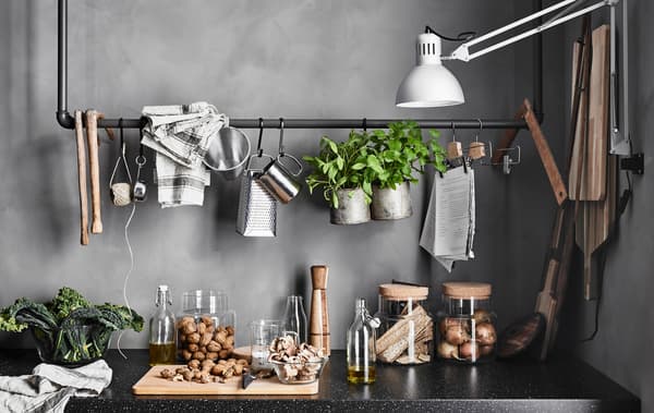 Un binario ottenuto da vecchi tubi con utensili da cucina e oggetti decorativi appesi sopra al piano di lavoro con contenitori in vetro per il cibo - IKEA.