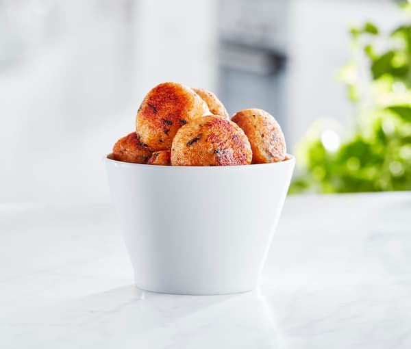 Un bol blanc sur un comptoir de cuisine contenant des boules de saumon rose fries et des herbes d'assaisonnement.