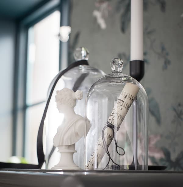Un bougeoir et deux cloches en verre MORGONTIDIG de dimensions différentes avec des décorations évocatrices de la musique à l’intérieur, sur une armoire.