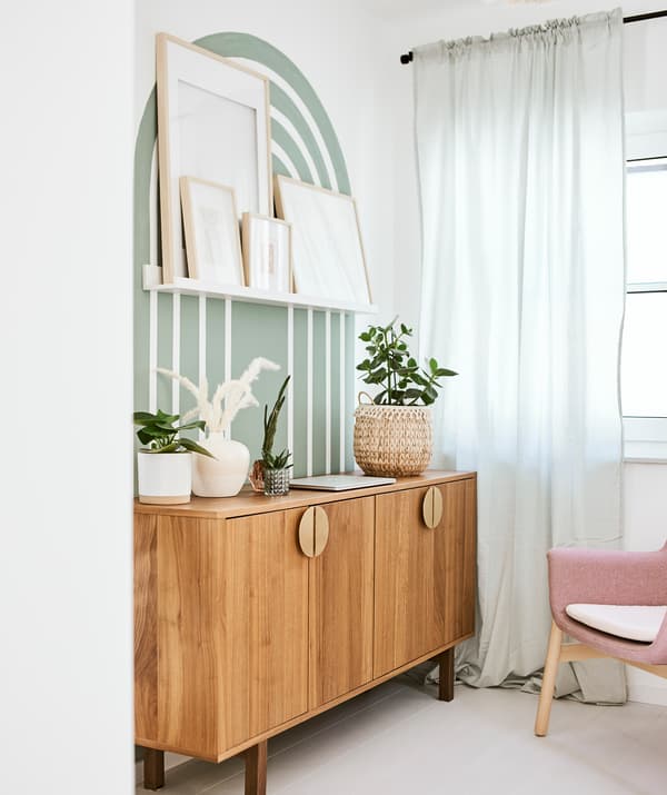 Un buffet de style moderne du milieu du siècle dernier adossé à un mur sur lequel a été peinte une arche verte, avec une étagère pour photos sur laquelle sont posées des œuvres d’art encadrées.