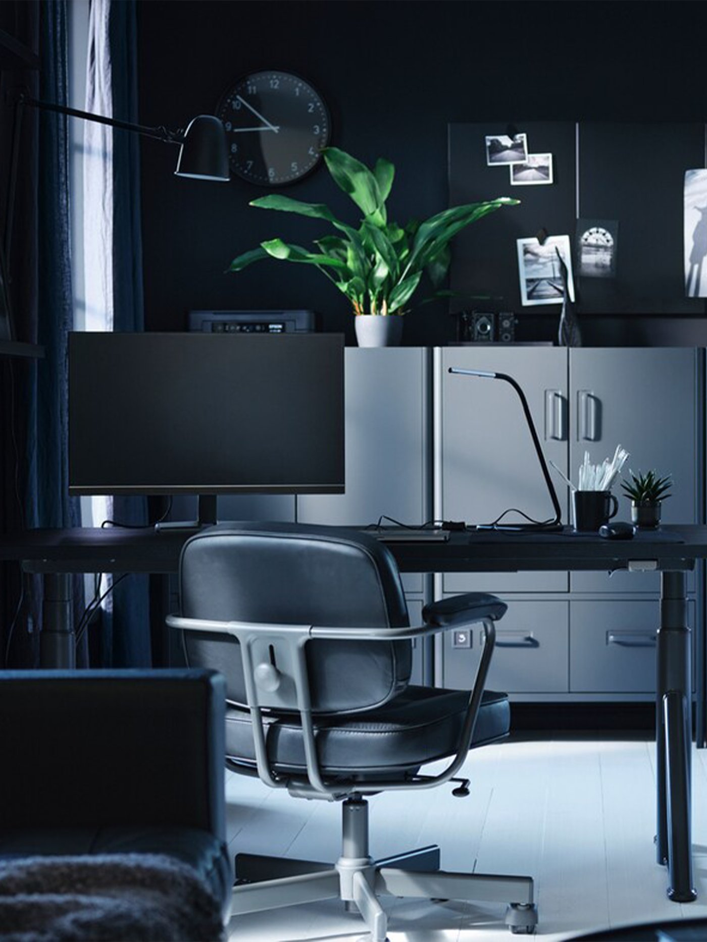Un bureau à domicile élégant aux tons sombres, avec un espace de travail moderne, une chaise ergonomique et une plante verte luxuriante.