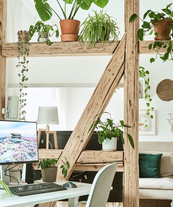 Un bureau à domicile séparé de la salle de séjour par des poutres en bois, des plantes et un store qui descend pour créer un écran.
