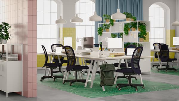 Un bureau clair et aéré avec plusieurs chaises de bureau FLINTAN noires autour d’un groupe de bureaux TROTTEN formant un espace partagé.