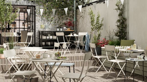 Un café extérieur avec des tables et des chaises pliables en acier beige, des fanions blancs, un plancher carrelé et un comptoir de service.