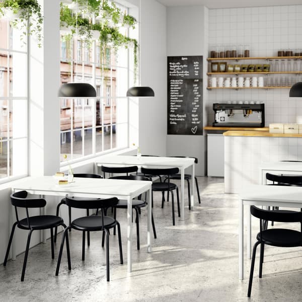 Un café lumineux avec des tables TOMMARYD, des chaises anthracite, une zone de comptoir avec une machine à café et un menu noir et blanc.