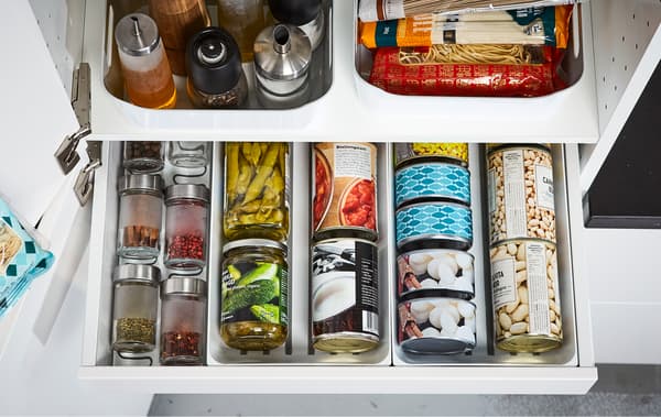 Un caixón de despensa IKEA MAXIMERA branco aberto amosando latas, especias e aceites ben organizados.