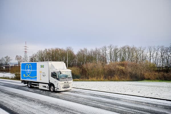 Un camion IKEA blanc affichant une publicité circule sur une route enneigée, dans un paysage hivernal avec des arbres dénudés en arrière-plan.