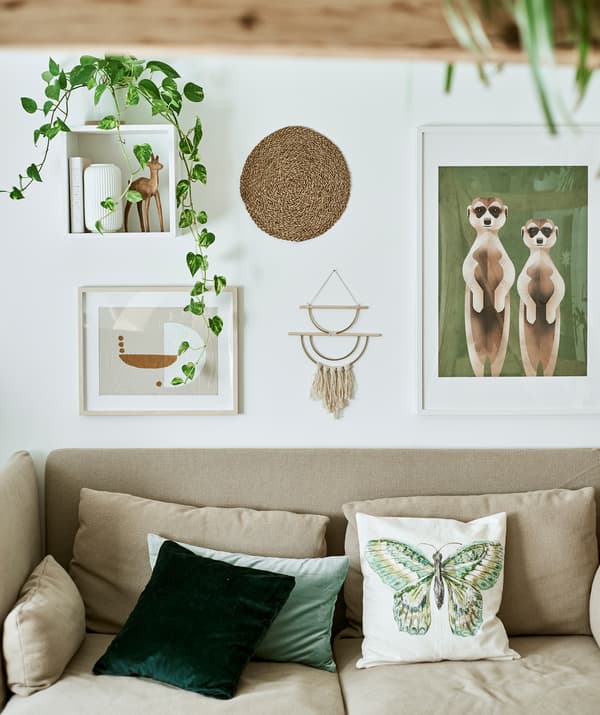 Un canapé à dossier haut avec des coussins verts contre un mur blanc avec une série d’illustrations encadrées, des décorations murales et des plantes.