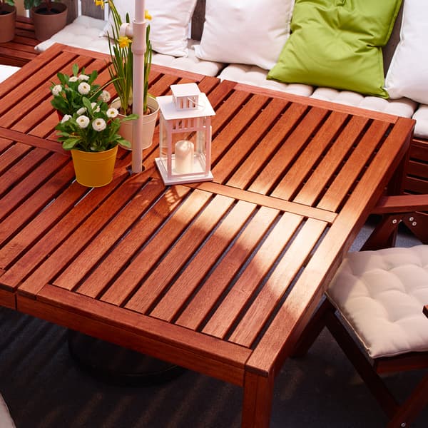 Un canapé blanc avec des oreillers et une table d'extérieur carrée en bois d'acacia marron avec des décorations sur le dessus.
