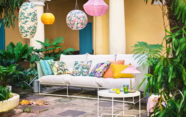 Un canapé blanc dans un patio en pierres naturelles. Les coussins sur le canapé et les suspensions au-dessus sont de couleurs vives et à motifs colorés.