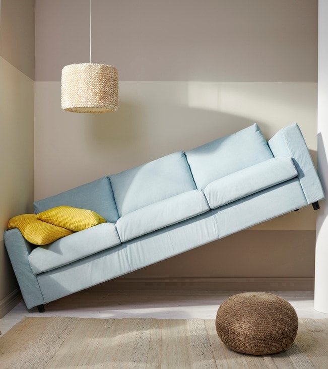 Un canapé bleu clair est bloqué en biais entre deux murs, avec un côté relevé contre un mur, car il est trop long.