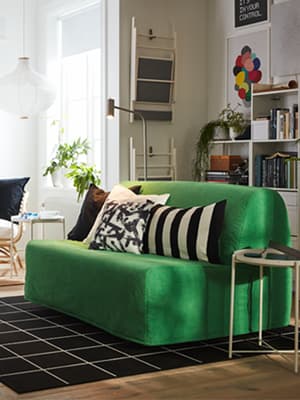 Un canapé lit LYCKSELE vert positionné au centre d'un studio, séparant la cuisine et le salon.