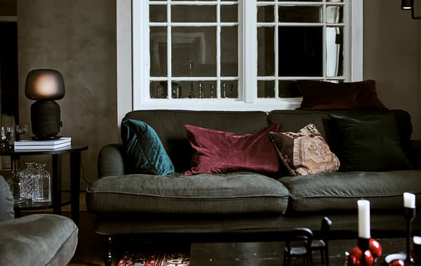 Un canapé vert avec des coussins aux couleurs de bijoux dans un salon avec une fenêtre d’intérieur, une table basse avec une lampe de table et un tapis persan.