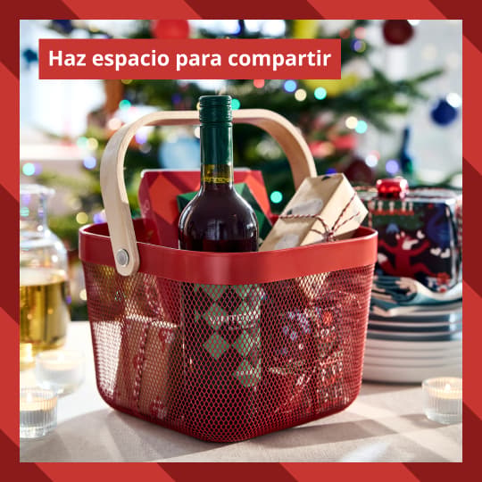 Un canasto IKEA con una botella de vino y comestibles adenro, sobre una mesa de comedor navideña.
