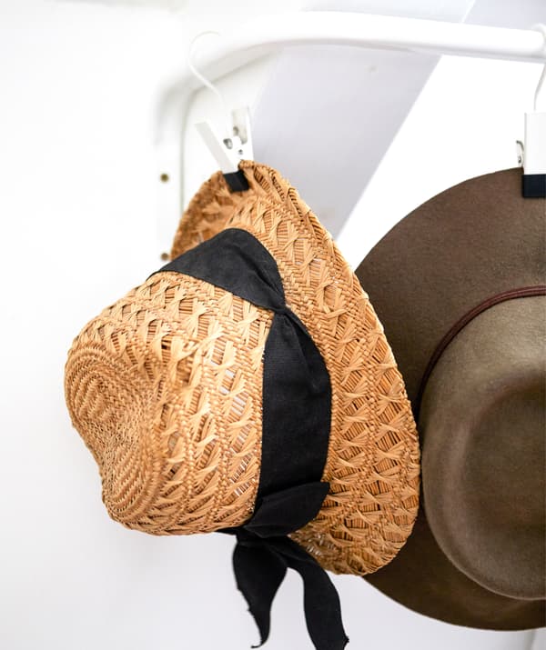 Un cappello di paglia appeso a un gancio su un bastone appendiabiti contro una parete bianca - IKEA