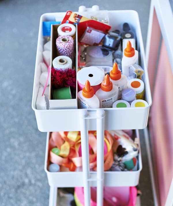 Un carrello bianco a tre ripiani con nastri colorati, colla e altri materiali artistici - IKEA