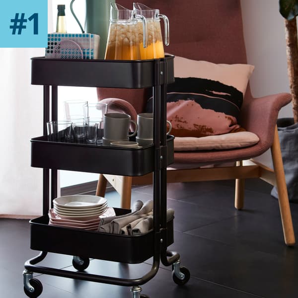 Un carrello nero RÅSKOG con brocche, piatti, bicchieri e tazze.