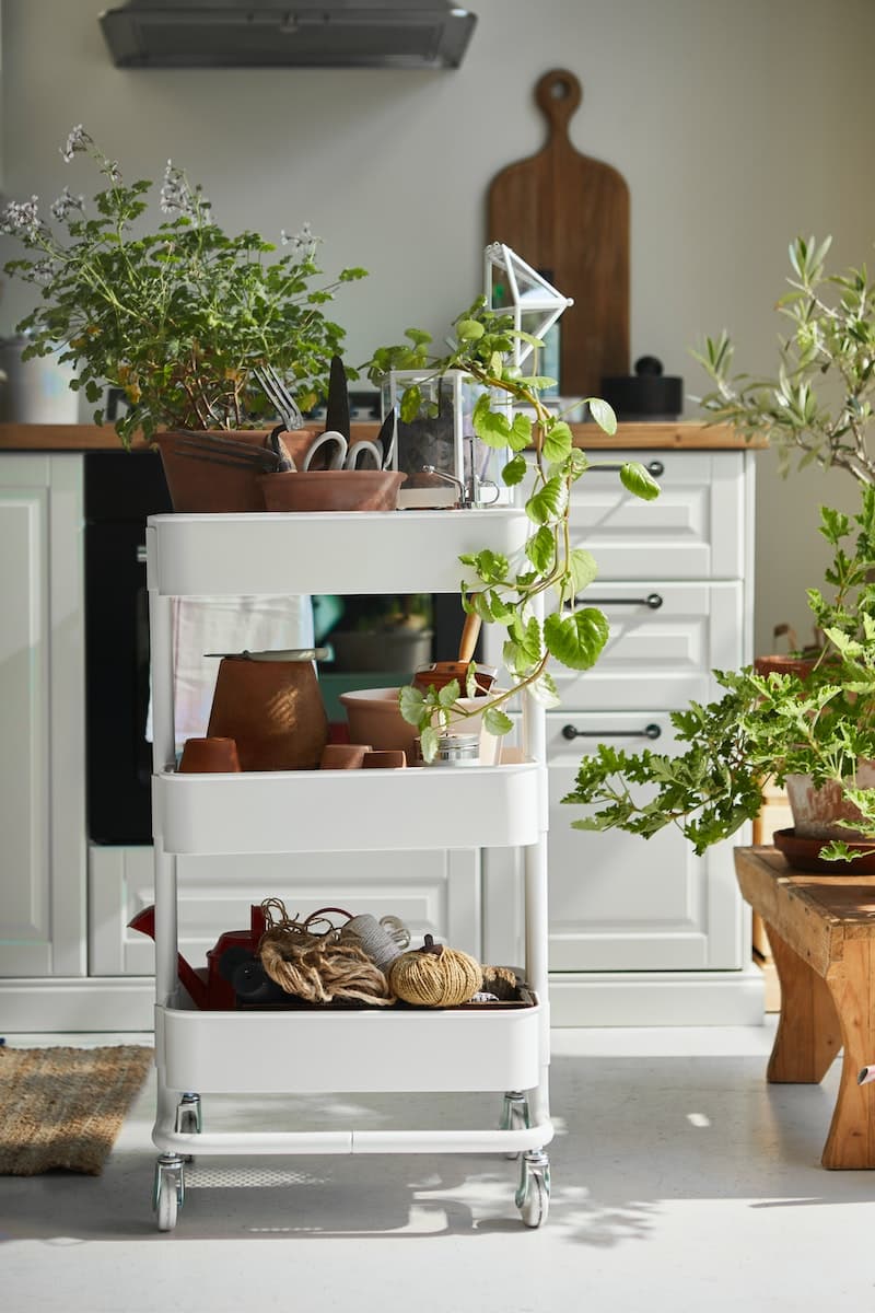 Un carrito RÅSKOG blanco con plantas en cada una de sus bandejas.