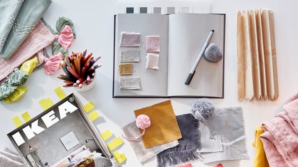 Un catalogue IKEA avec marque-pages, des crayons de couleurs dans un pot et des échantillons de tissu multicolores.