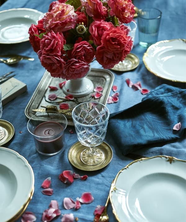 Un centrotavola di rose su una tovaglia blu, insieme a una candela, piatti e bicchieri.