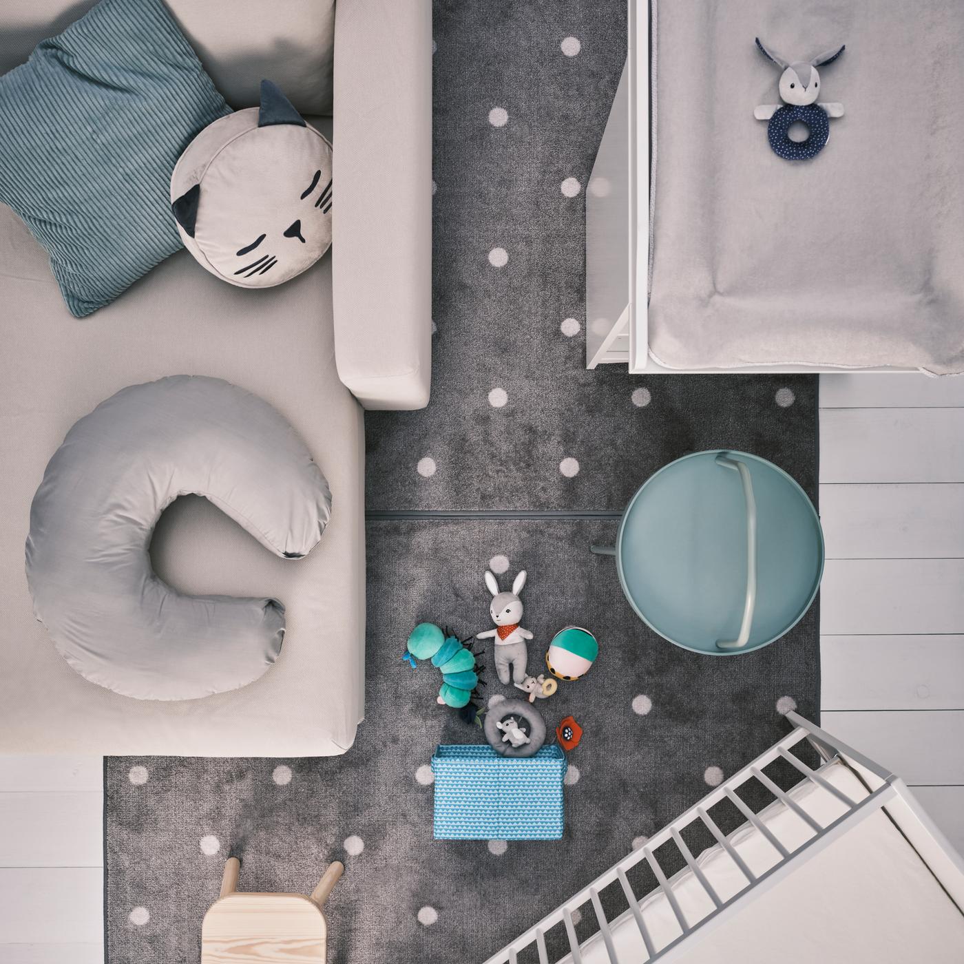 Un chaise longue beige con cojines, un cambiador SMÅGÖRA blanco y una cuna, además de un taburete para niños FLISAT sobre una alfombra gris.