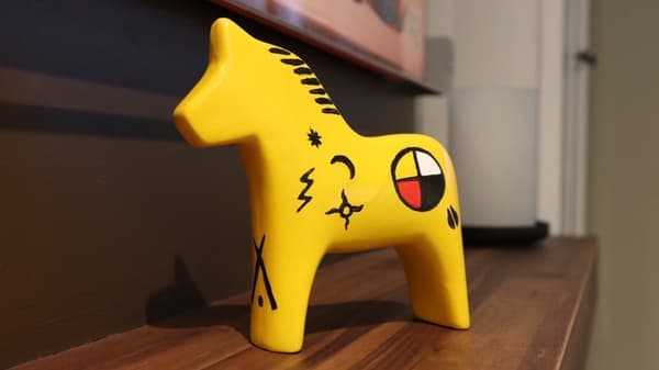 Un cheval de Dalécarlie jaune, orné de motifs noirs sur le flanc, est posé sur une table en bois.