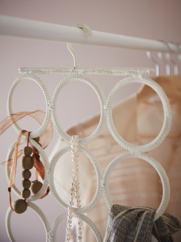 Un cintre multi-support KOMPLEMENT avec des colliers, un foulard et d’autres accessoires est accroché à une tringle de garde-robe.