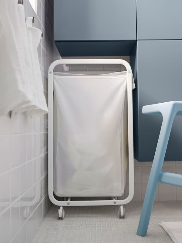 Un cistell de la bugada blanc a l'espai entre l'armari i la paret d'un bany petit.