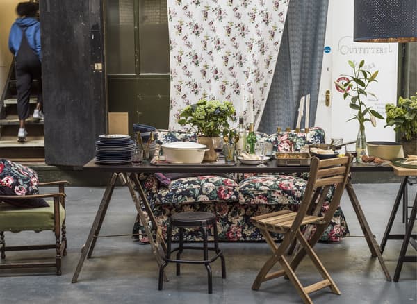 Un coin repas avec des chaises dépareillées, des plantes et un canapé à motif floral.