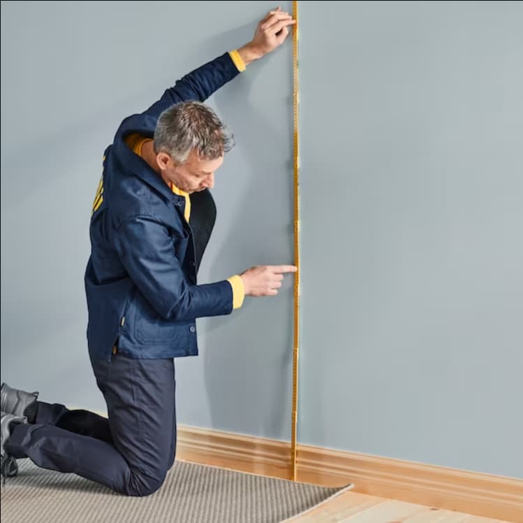 Un colaborador de IKEA agachado midiendo una altura en un muro de color gris.