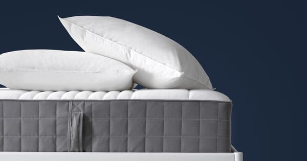 Un colchón con lados grises y dos almohadas encima sobre un fondo azul.