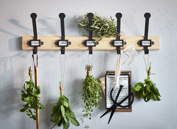 Un colgadoiro de piñeiro IKEA KARTOTEK empregado como herbario, con cinco ganchos negros para colgar herbas e tesoiras.