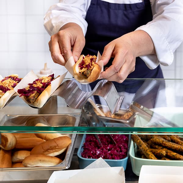 Un collaborateur du bistro IKEA place un hot-dog végé sur un plateau métallique ondulé.