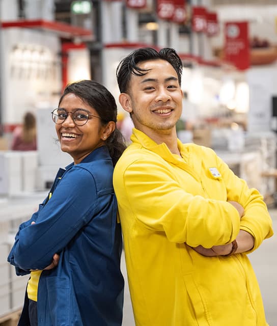 Un collaborateur et une collaboratrice IKEA dos à dos les bras croisés et souriants